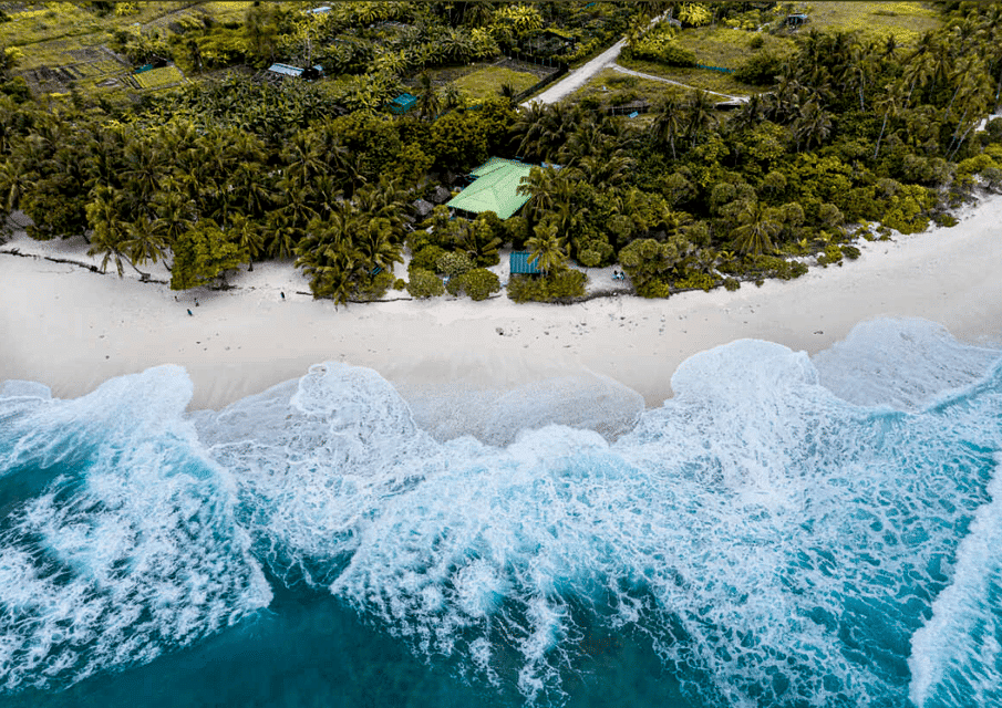 A picturesque view of Fuvahmulah Thoondu, featuring its unique white pebble beach against the backdrop of turquoise waters and a serene hori