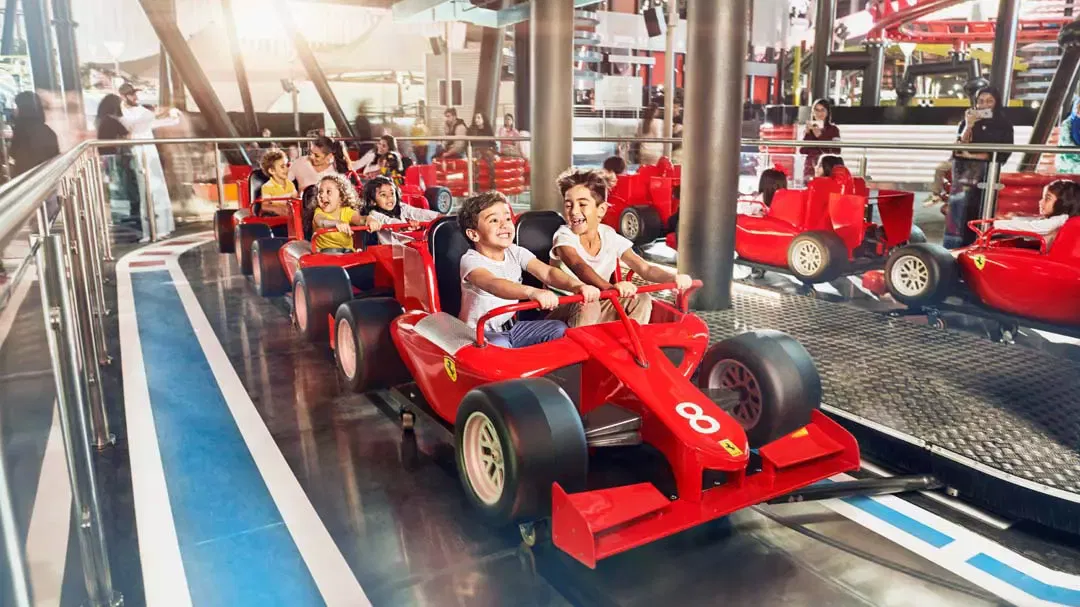 Young children driving miniature red Formula One cars along a marked indoor track at the junior driving school at Ferrari World Abu Dhabi