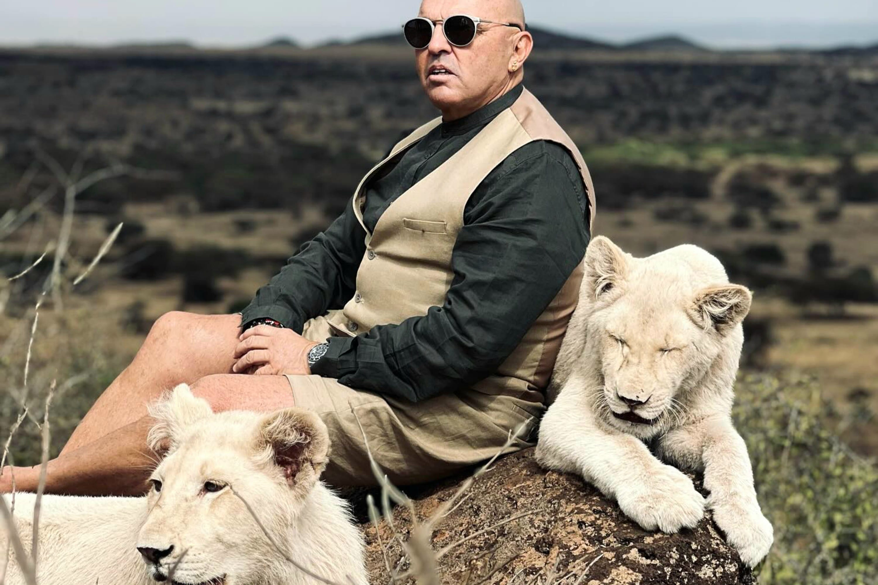 ​A high-end guest posing with two white lions in a private wildlife sanctuary.