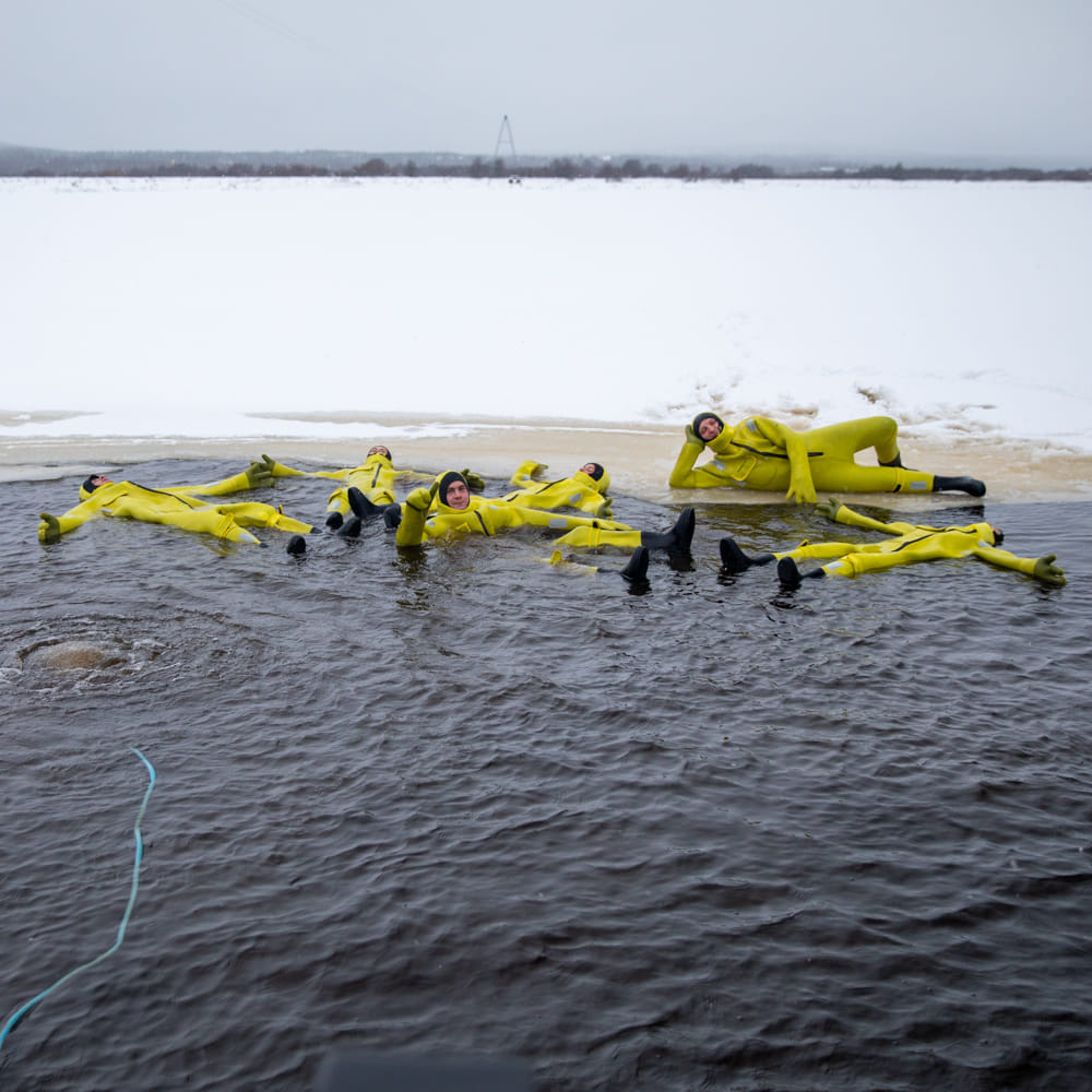 People floating in frozen river with immerion suits at Roiske Arctic Sauna Experience