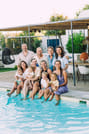 A close-up group photo of a family smiling together next to a blue swimming pool.