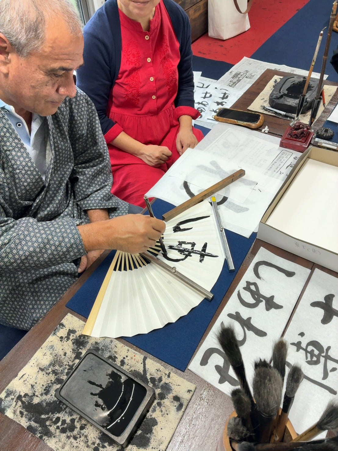 Close-up of a guide assisting a guest in writing Japanese characters on a folding fan with brush and ink