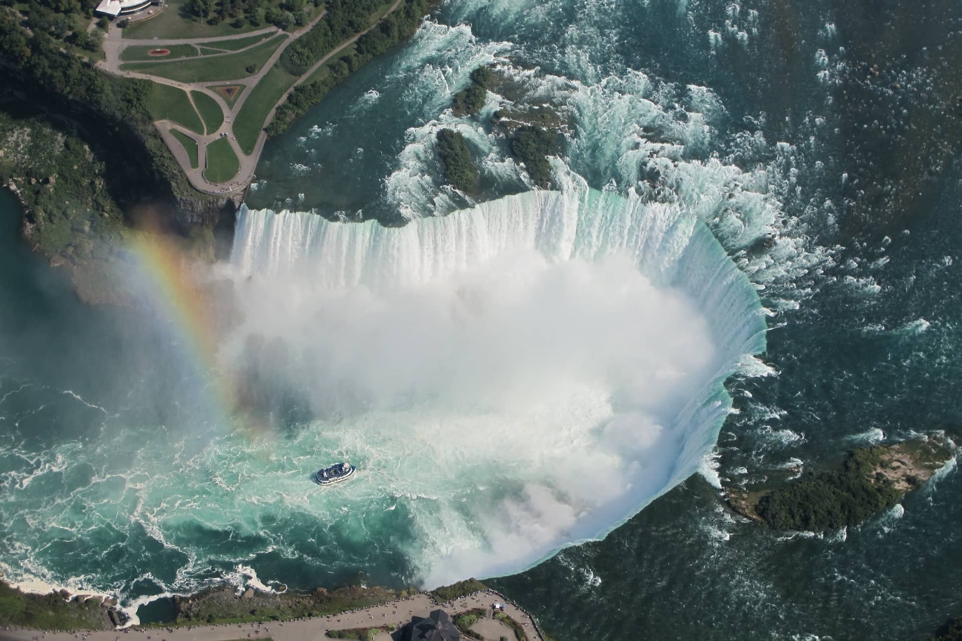 Aerial view of Niagara Falls with mist, rainbow, and tour boat below the cascading water