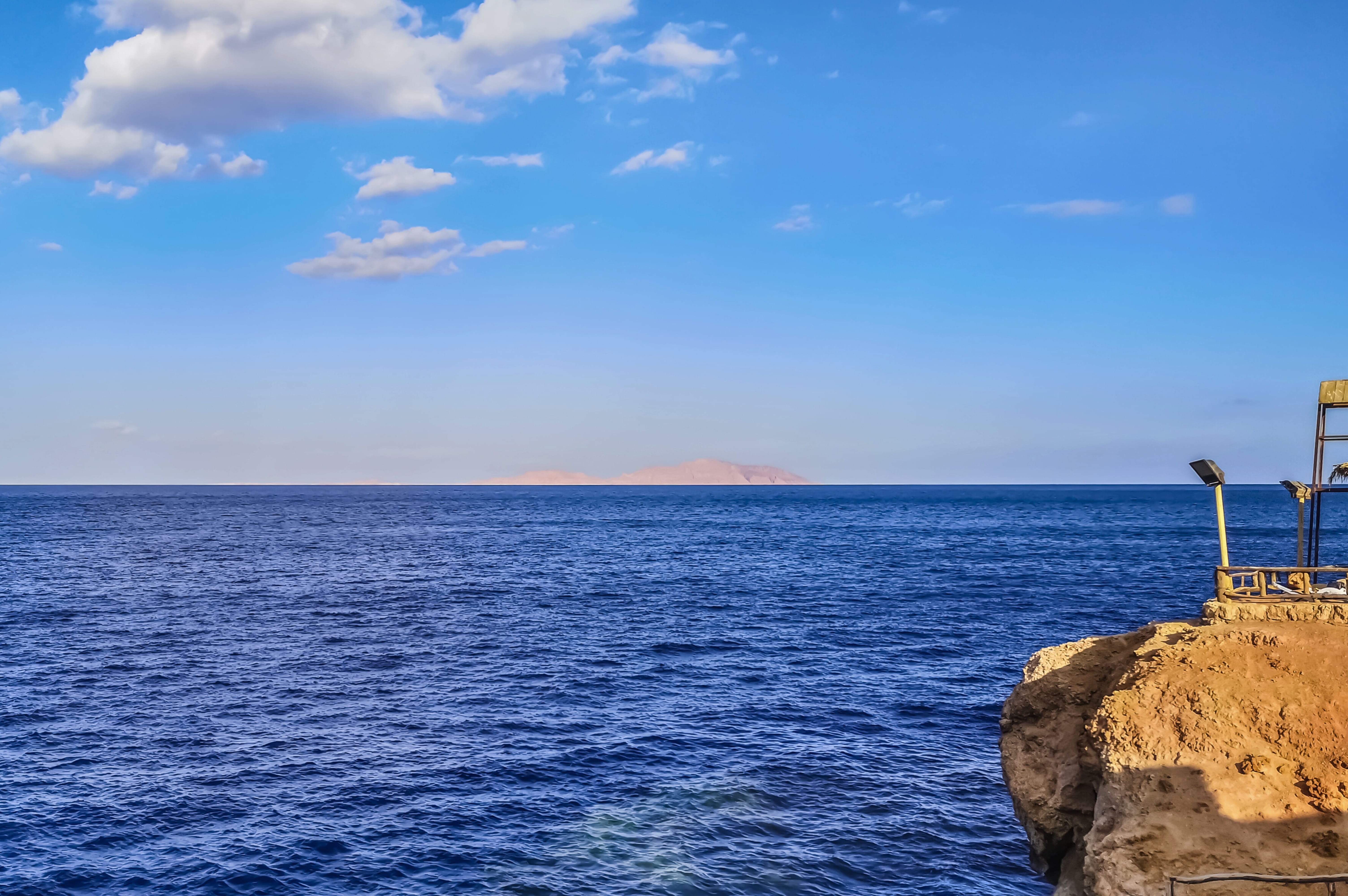 A rocky cliffside viewpoint overlooking the vibrant blue waters of the Red Sea and Tiran Island in Sharm El Sheikh.