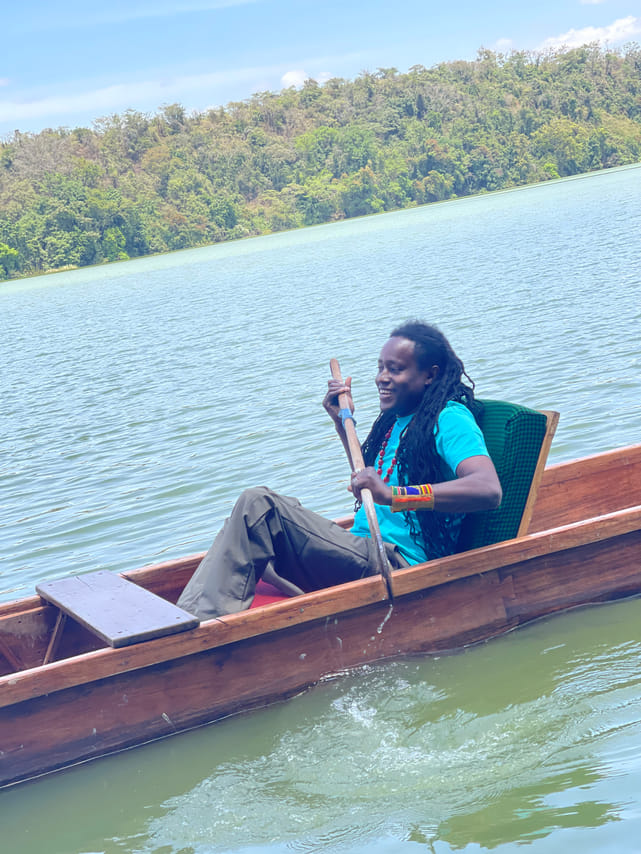 ​A man paddling a wooden canoe on Lake Duluti with green forest scenery in the background.