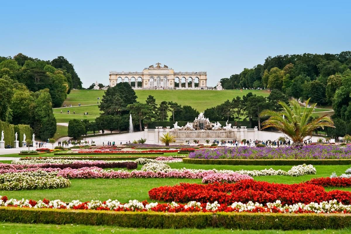 Colorful flower gardens and fountains leading up to the Gloriette pavilion in Schönbrunn Palace, Vienna, on a sunny day.