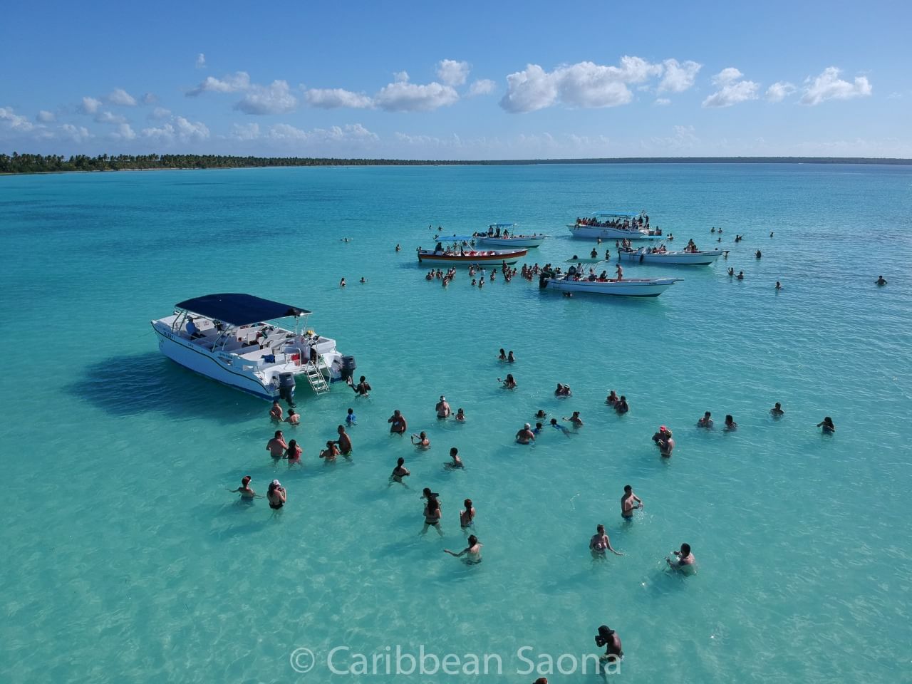 “Vista aérea de embarcaciones rodeadas de personas disfrutando de la Piscina Natural de Isla Saona, caracterizada por sus aguas cristalinas 