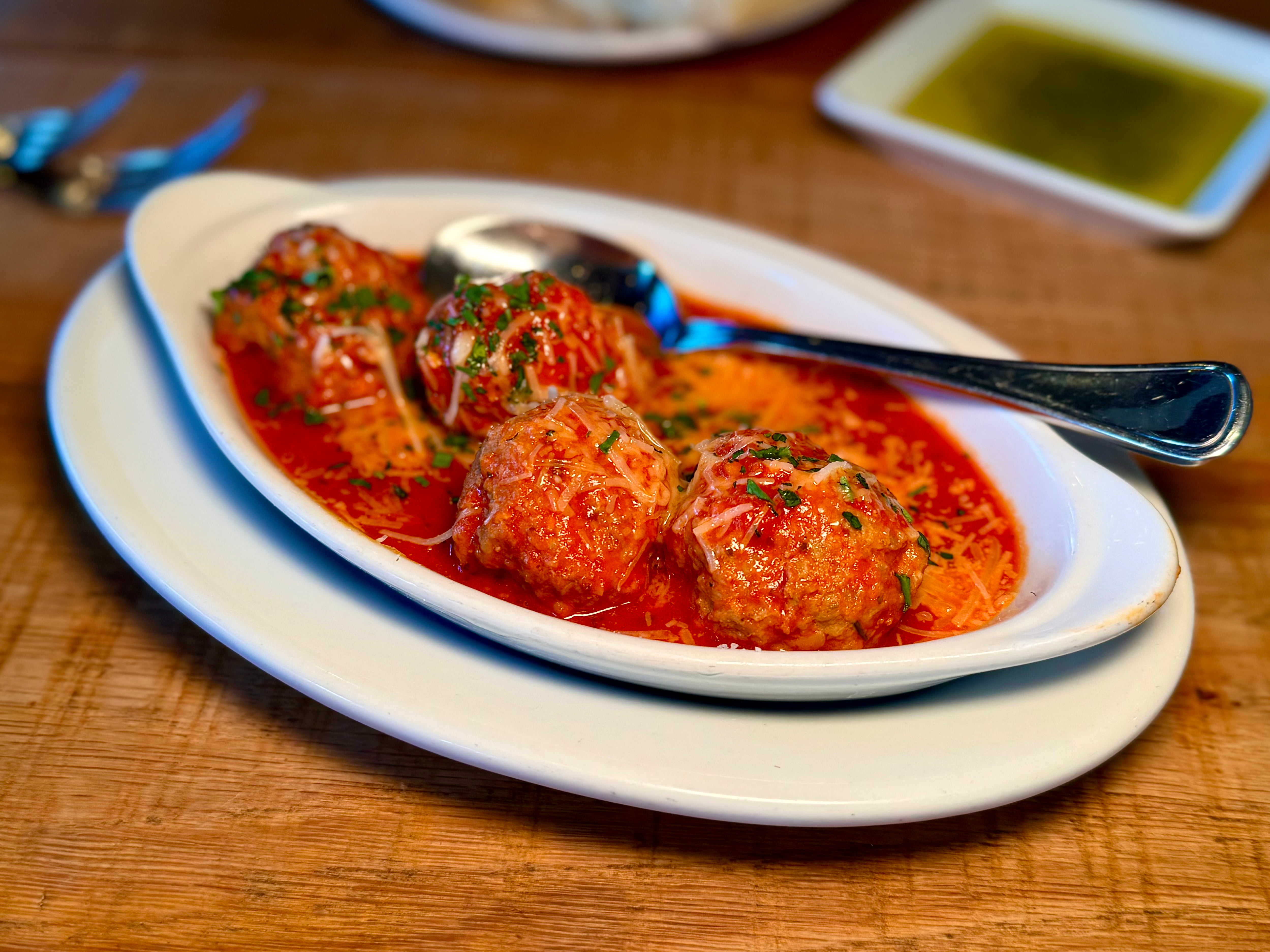 A plate of meatballs covered in marinara sauce and grated cheese.