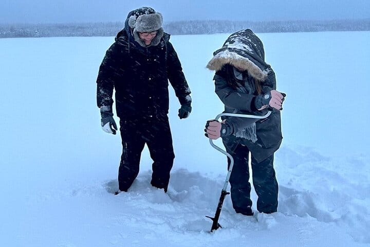 Guests drilling for fish on a frozen lake during StayLapland’s Ice Fishing with Snowmobiles in Rovaniemi.
