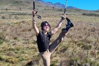 A happy female hiker celebrating with trekking poles raised high on a scenic trail of Mount Kilimanjaro.