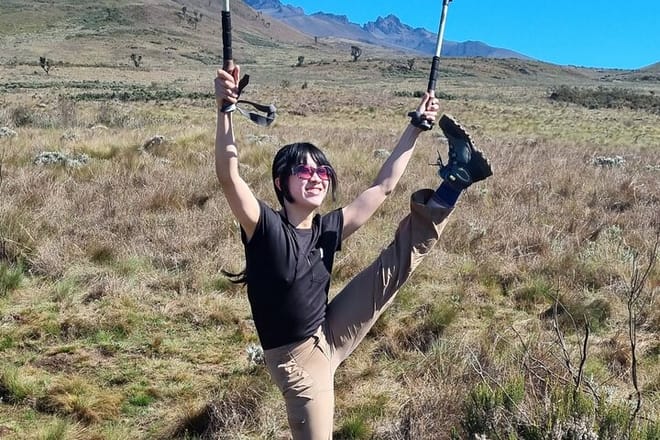A happy female hiker celebrating with trekking poles raised high on a scenic trail of Mount Kilimanjaro.