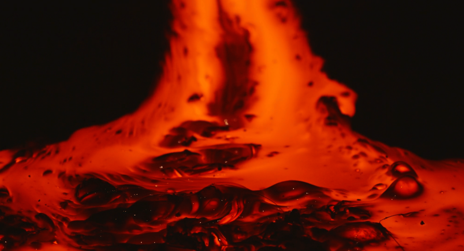 A close-up view of molten lava bubbling and flowing in vivid shades of red and orange against a dark background, showing its texture and hea