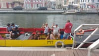 Guests waving from yellow moliceiro boat on Aveiro canal beside boarding dock