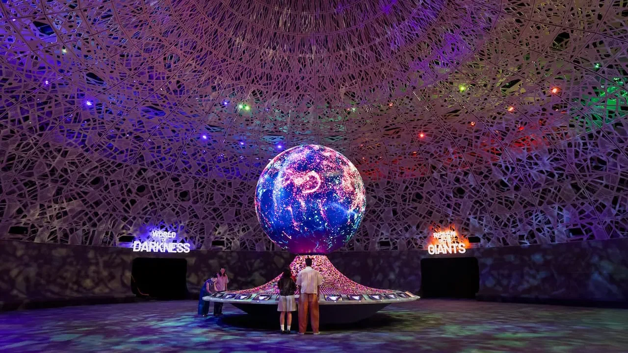 Visitors stand in a large round hall beneath a patterned dome, facing a glowing globe that displays a digital map at Exploria in Mandai Singapore Ticket.