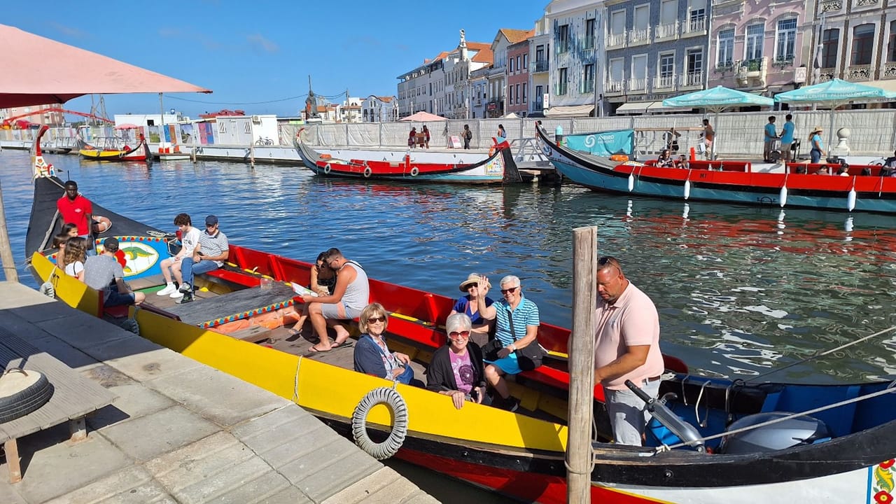 Guests seated in traditional moliceiro boat on Aveiro canal near colorful buildings