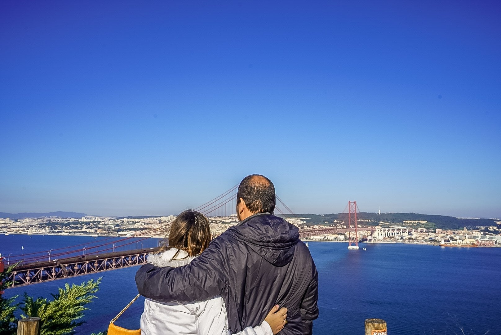 Two visitors looking at the Tagus river and the 25 de Abril Bridge from a Lisbon viewpoint