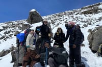 Diverse group of hikers in high-performance mountain gear smiling on the snowy trail of the Rongai Route.