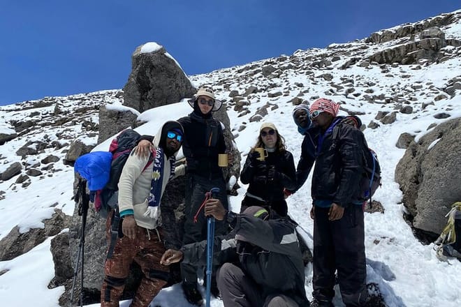 Diverse group of hikers in high-performance mountain gear smiling on the snowy trail of the Rongai Route.