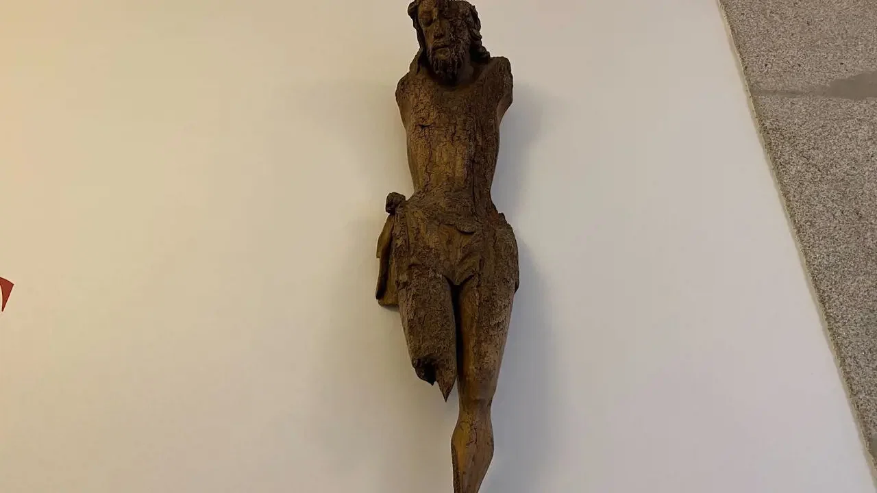 An aged, armless wooden crucifix figure is mounted on a plain white wall at Clérigos Tower & Museum Ticket.