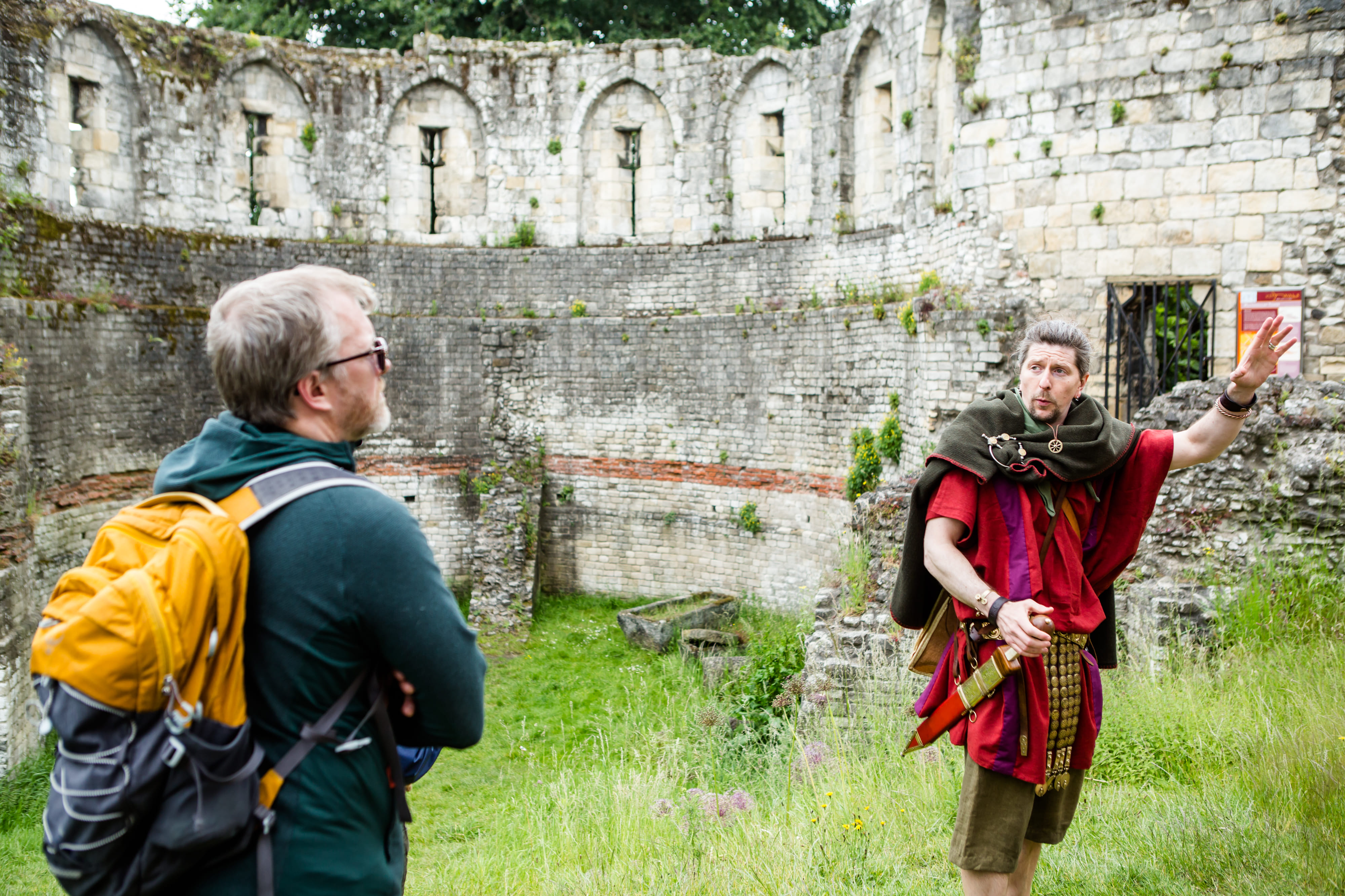 A Roman legionary talks to his group within the Multangular Tower. Ancient Roman, gritstone sarcophagi lay in the background. 