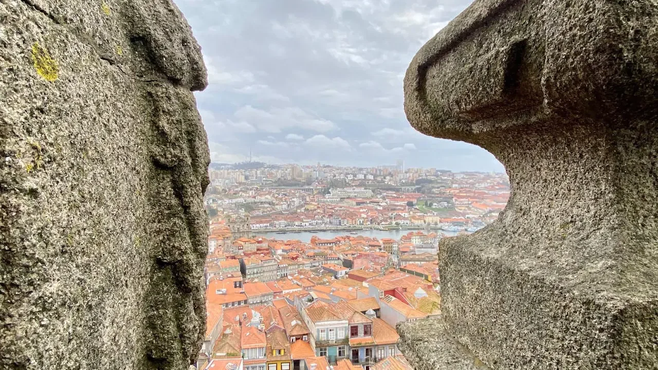 Framed by two weathered stone structures, a distant cityscape stretches out beneath a cloudy sky at Clérigos Tower & Museum Ticket.
