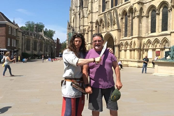 A Viking holds his big knife next to the throat of a smiling tourist from Australia, next to York Minster.