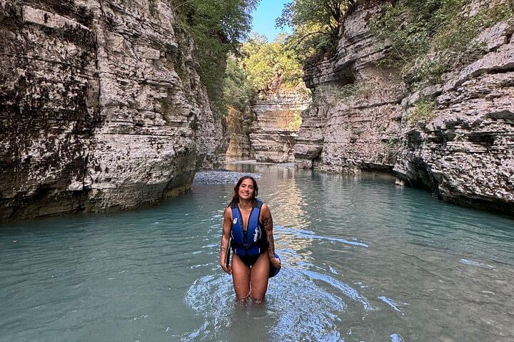A person in a life jacket standing in a scenic canyon , surrounded by rock formations and nature .