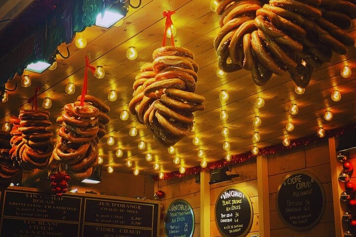 Bretzels empilés suspendus au plafond d'un chalet de marché de Noël. Des menus de vin chaud et de cidre sont visibles en bas.