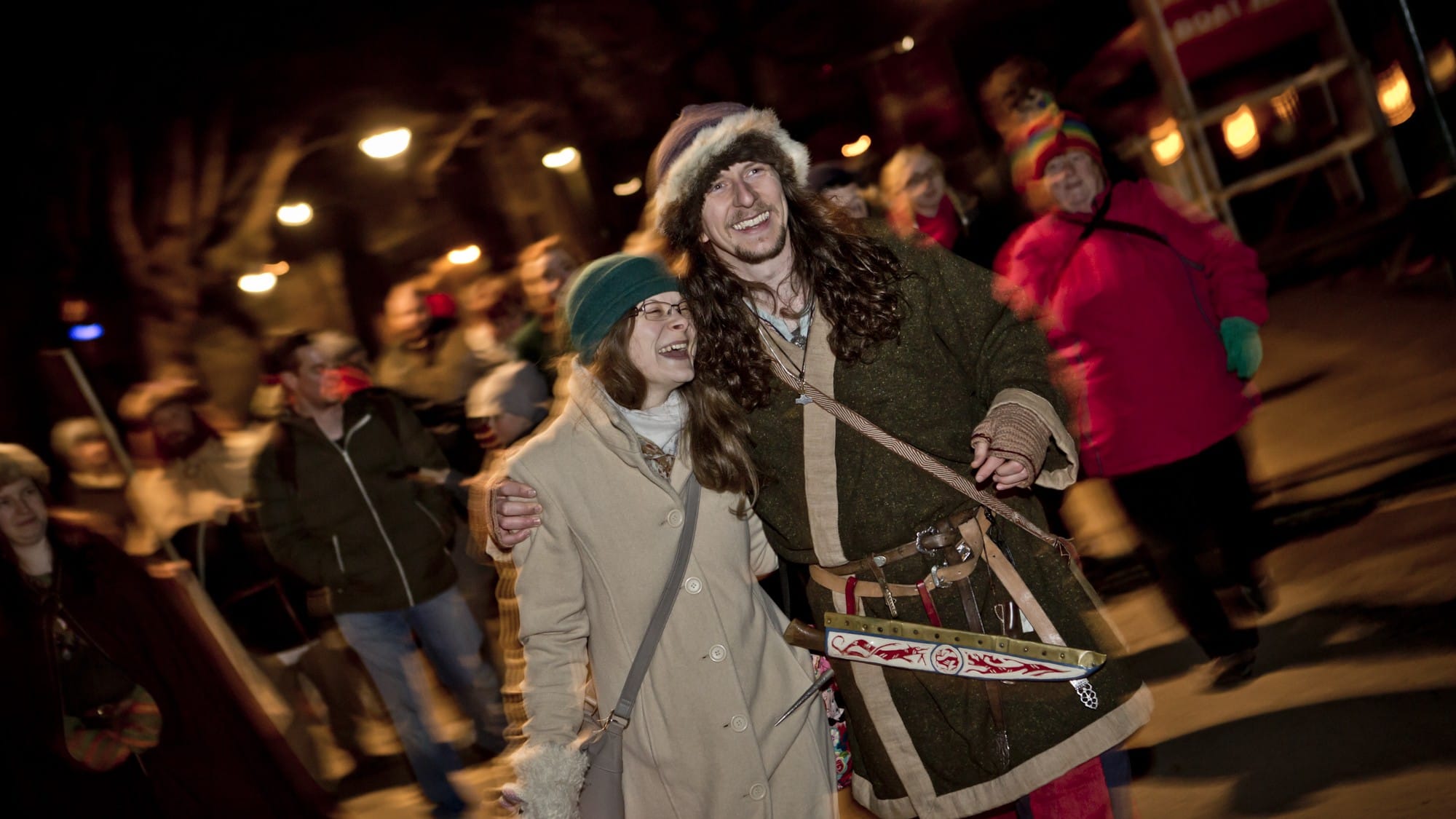 A Viking tour guide walking with his arm around a lady guest, they are both smiling and laughing happily.