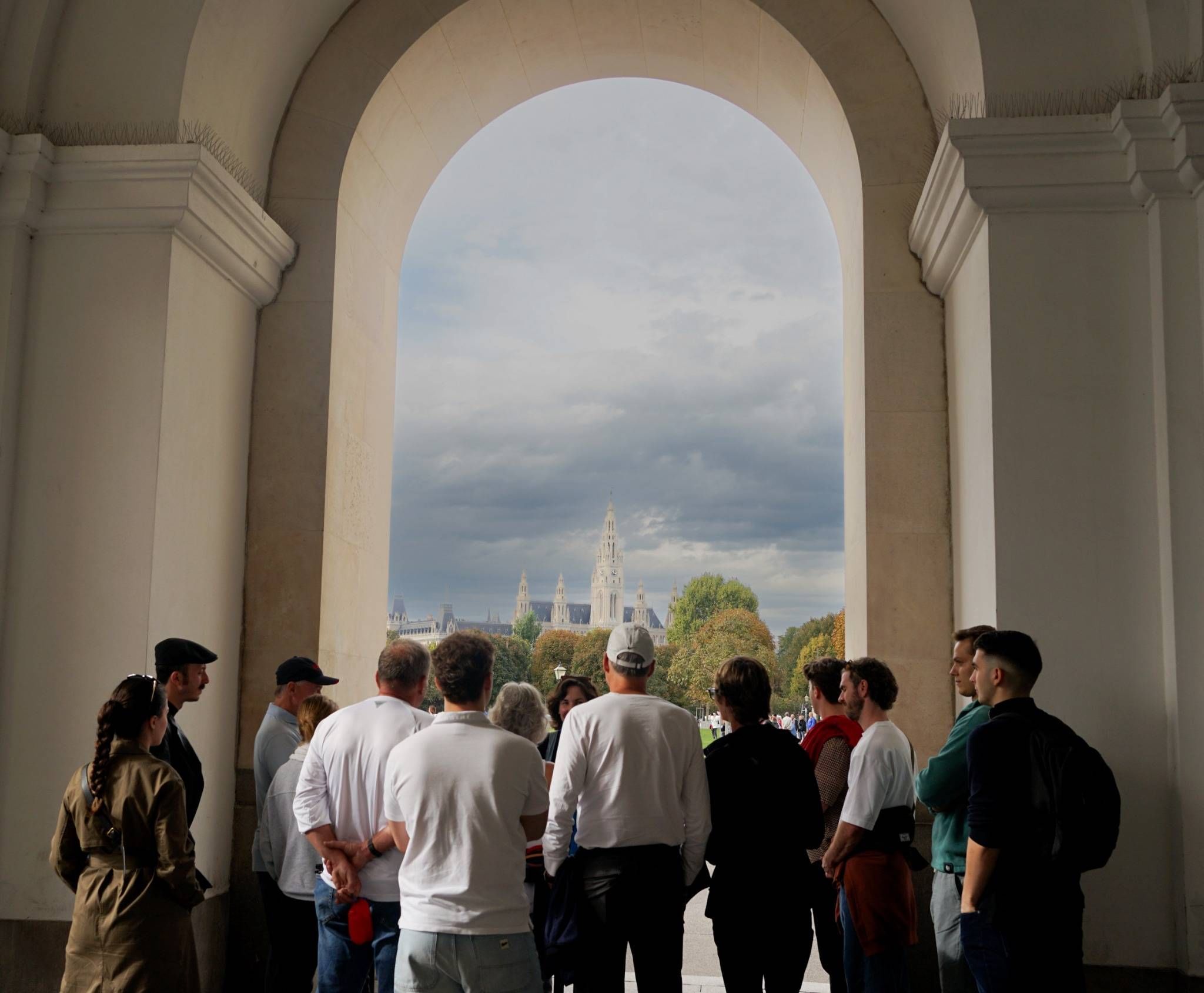 People standing under a tall stone arch, looking out toward Vienna’s City Hall across a park