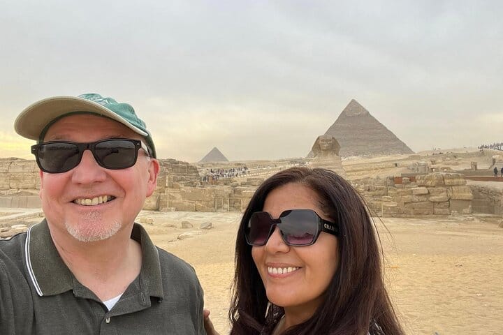 Tourist couple posing with their tour guide in front of the Pyramids of Giza