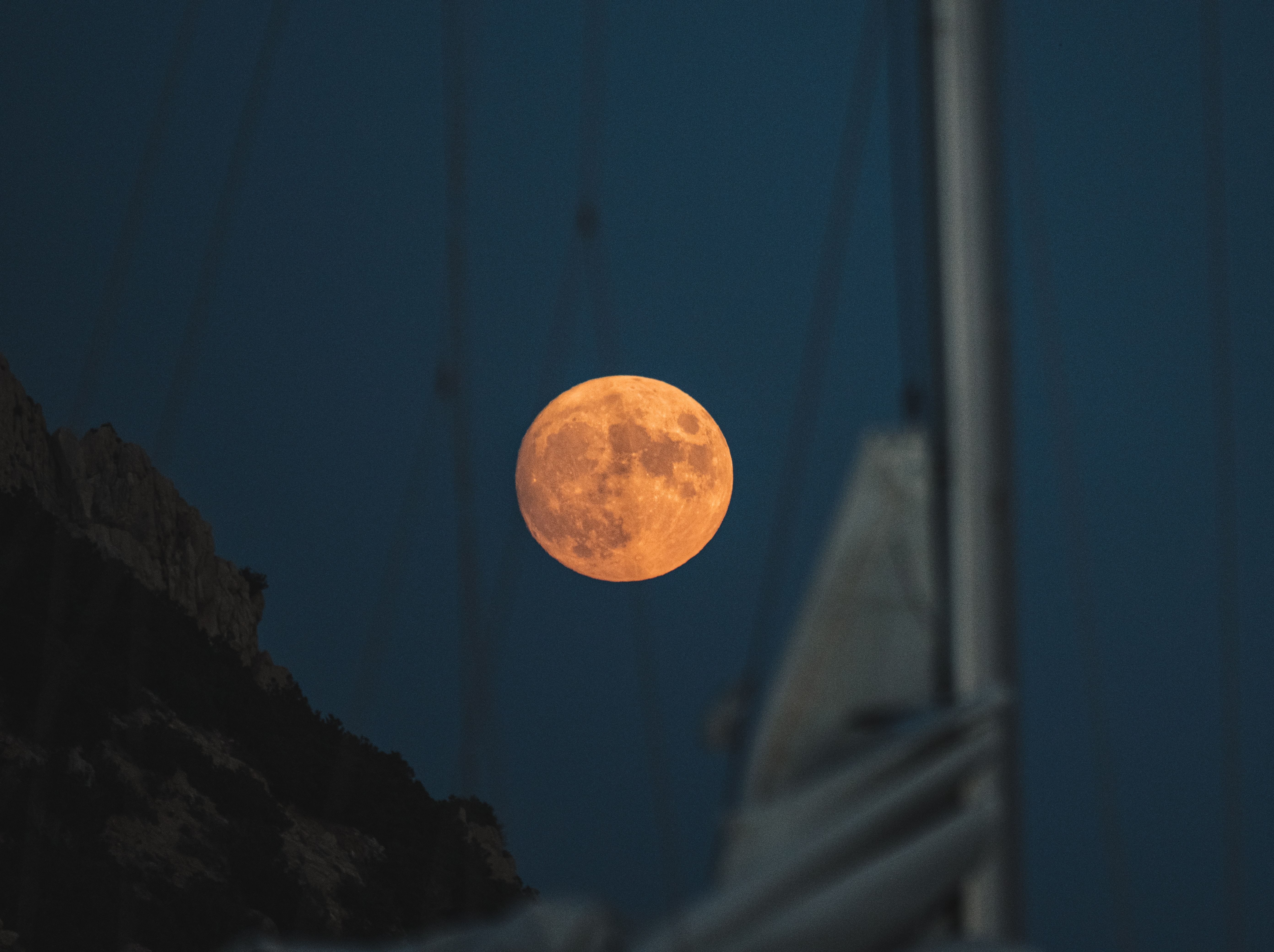 Close-up of the full Moon between a sailboat mast and its main sail.