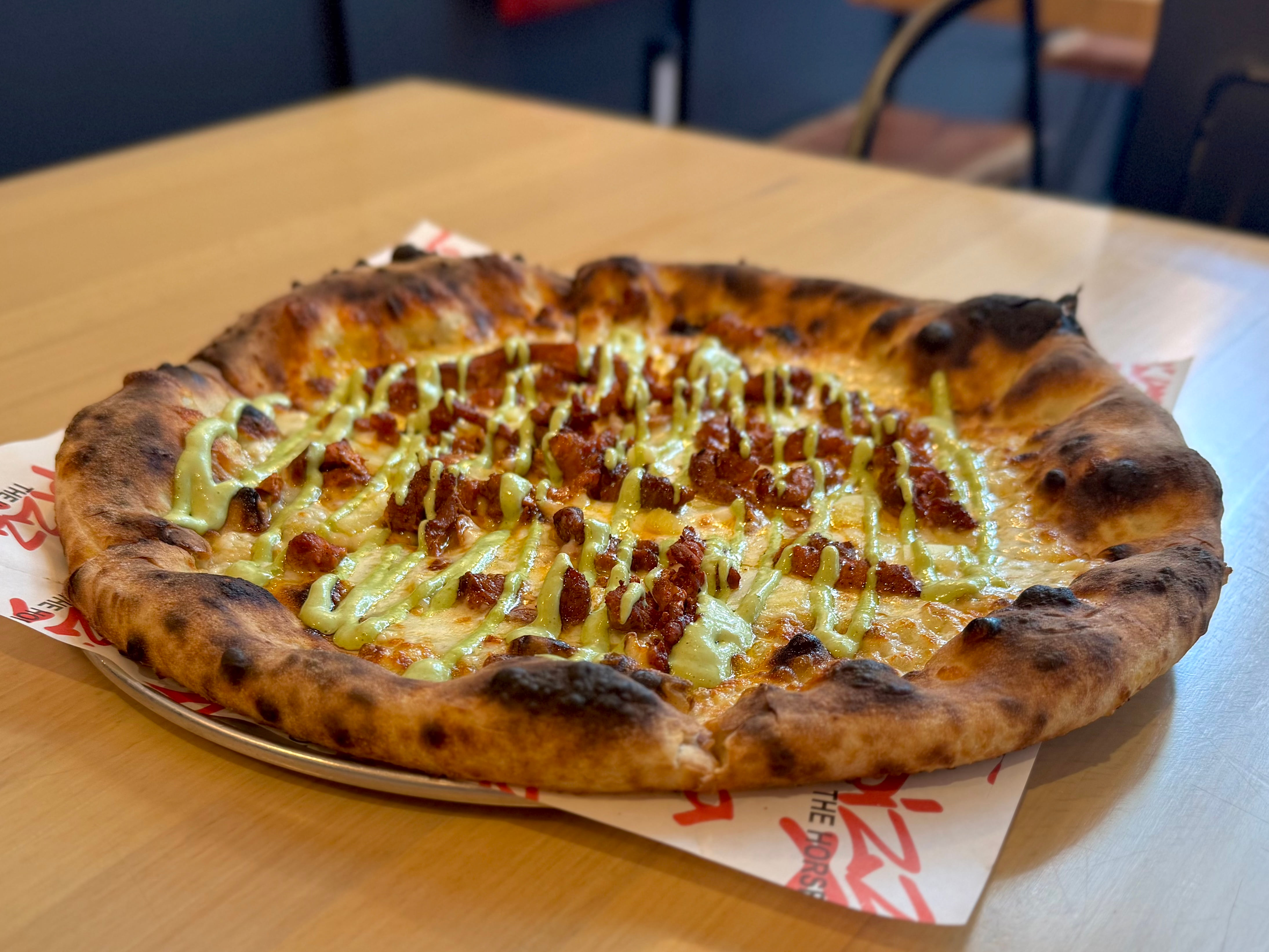 A Pizza Al Pastor topped with meat, pineapple, cheese, and herbs on a wooden table.