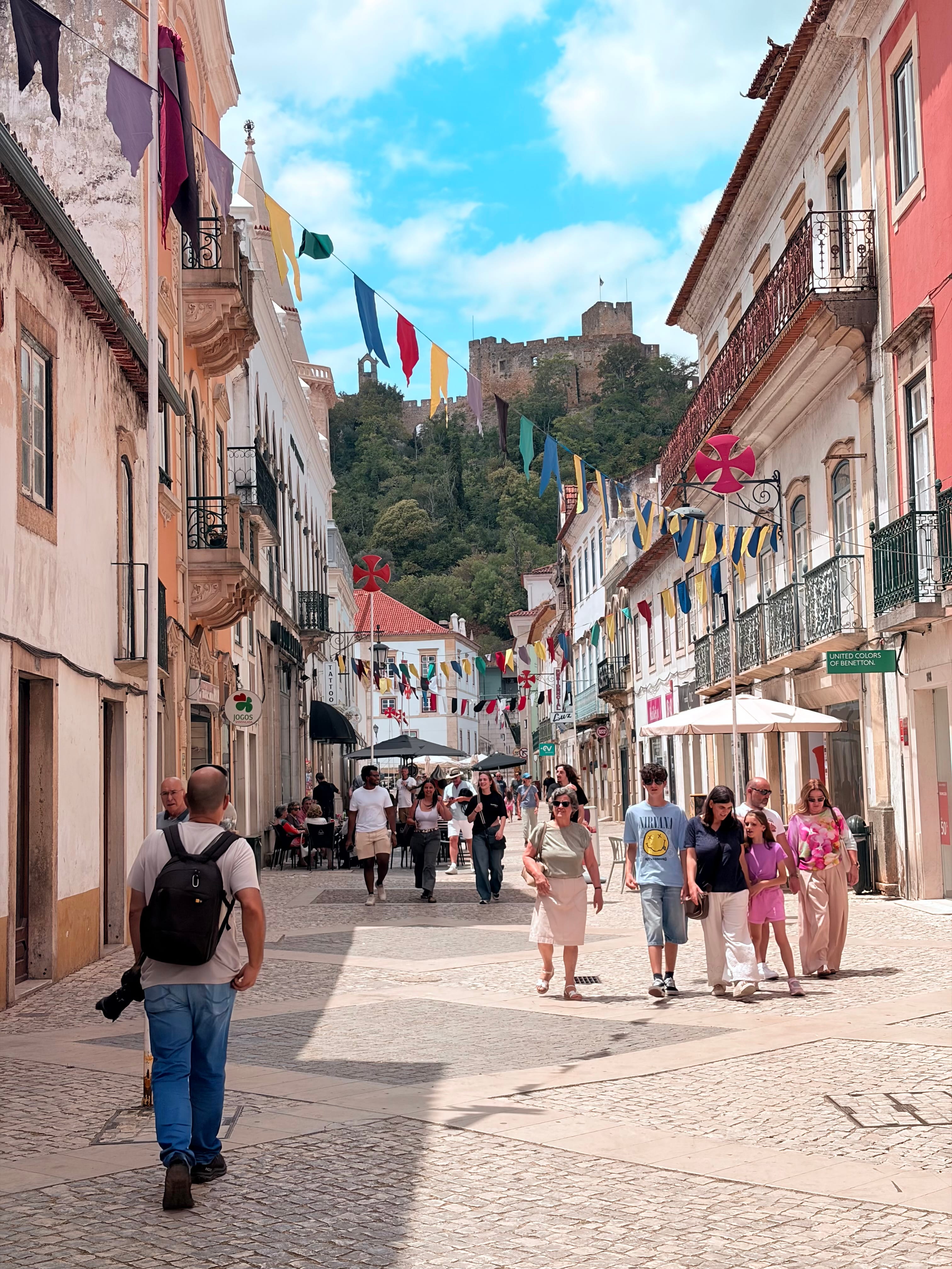 Rua pedonal no centro histórico de Tomar, com paralelepípedos tradicionais, edifícios históricos de fachadas coloridas e esplanadas de cafés