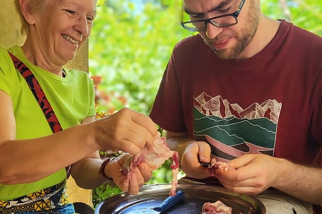 Close-up of two travelers engaged in a cooking activity, handling fresh food during a guided cultural tour.