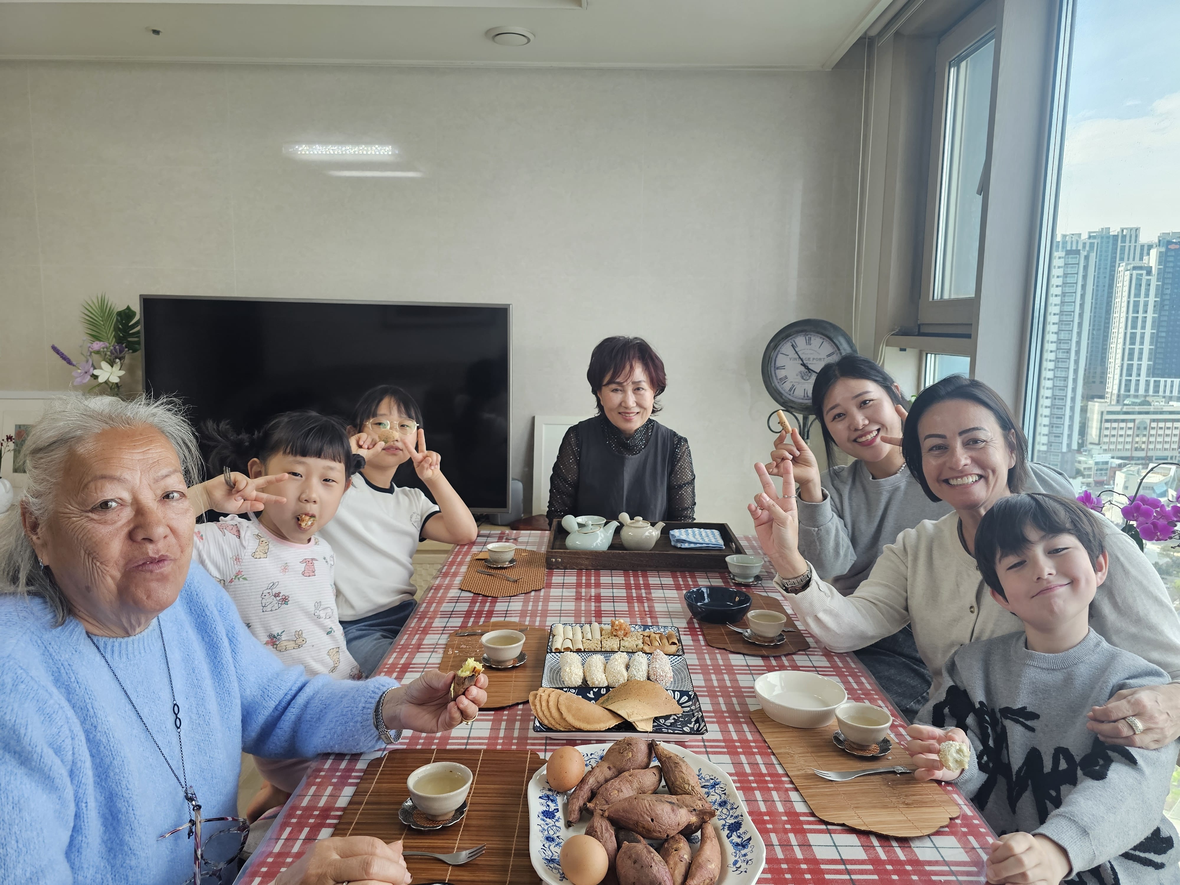 Guests enjoying tea and Korean snacks together in a cozy home setting, sitting around a table and sharing a warm moment
