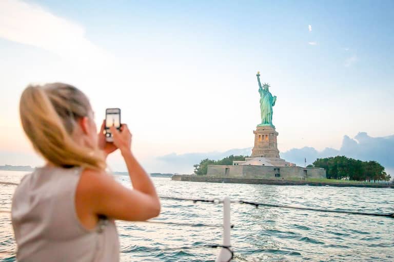 Tourist photographing the Statue of Liberty from a Manhattan harbor sightseeing cruise