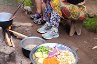 A platter of chopped onions, eggplant, carrots, and peppers near a cook fire.