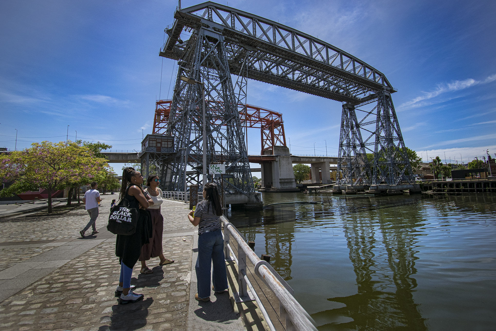Foto of the Bridge, in front is the river and you can see the side walk with some people on it on the left of the picture