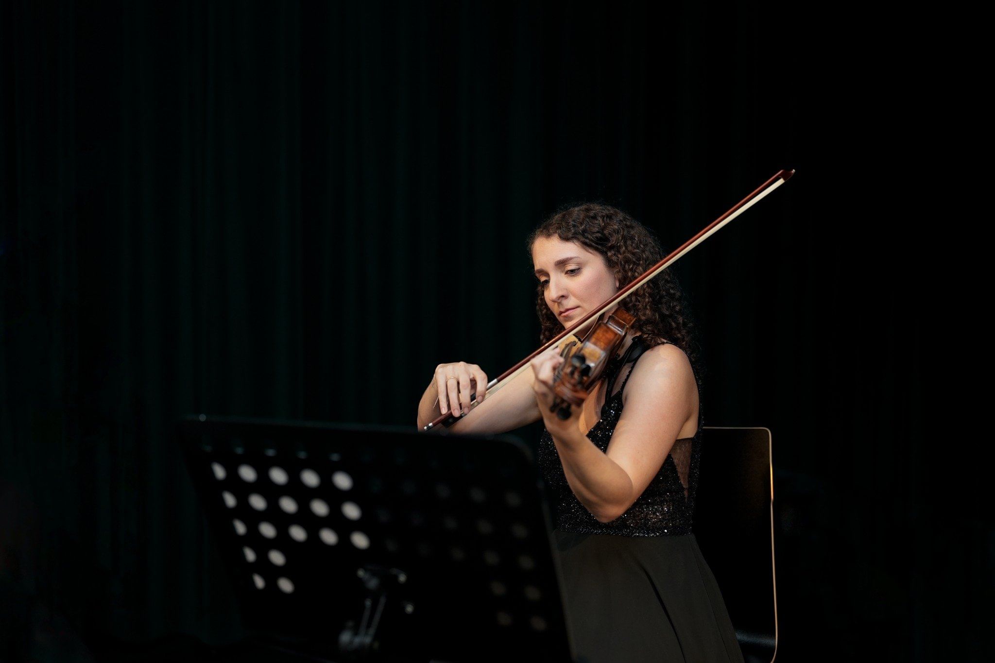 Female violinist in black dress playing at Haus der Musik, Vienna, seated with a music stand.