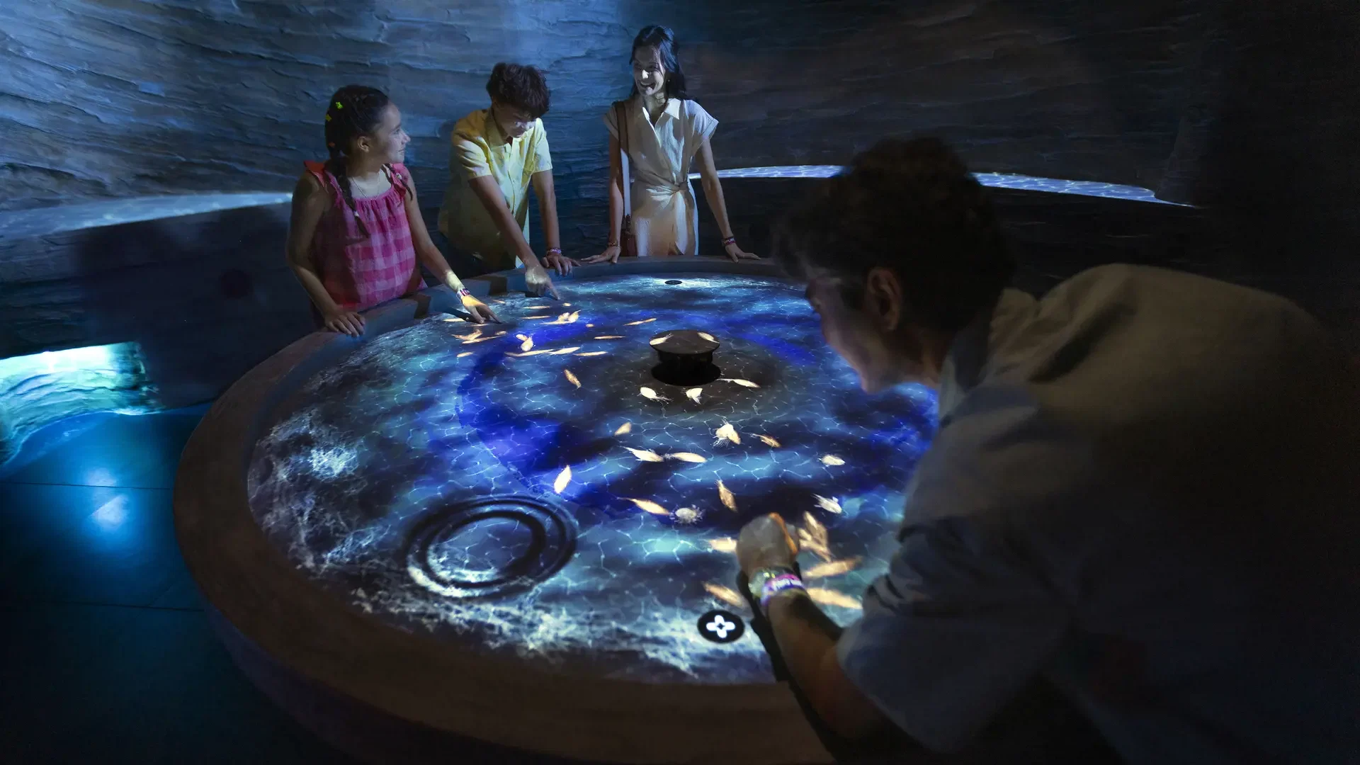 A family gathers around a circular interactive digital table displaying glowing sea life animations at Exploria in Mandai Singapore Ticket.