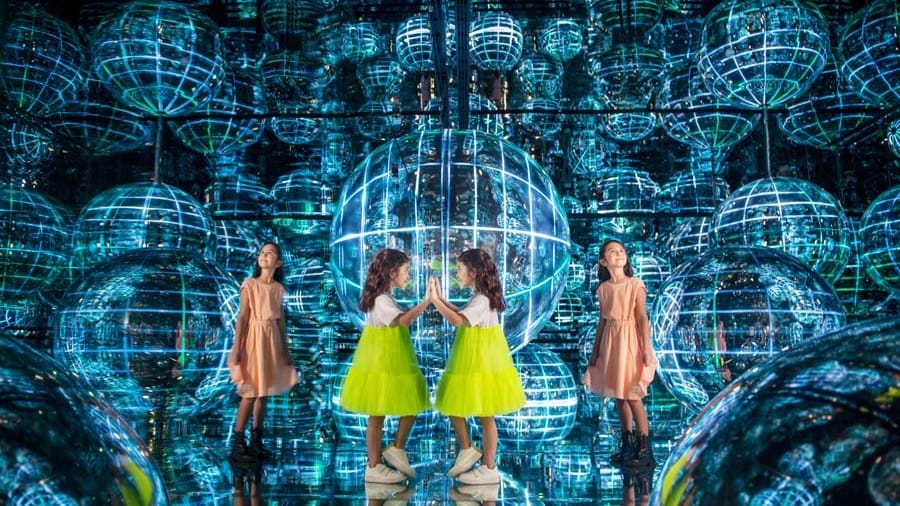 Children reflected repeatedly in a mirrored room filled with illuminated blue wireframe spheres at AYA Universe Dubai