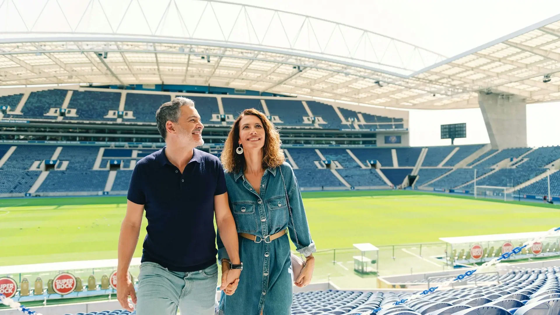 A man and a woman hold hands as they walk through the stands of a large stadium at FC Porto Museum & Dragão Stadium ticket.