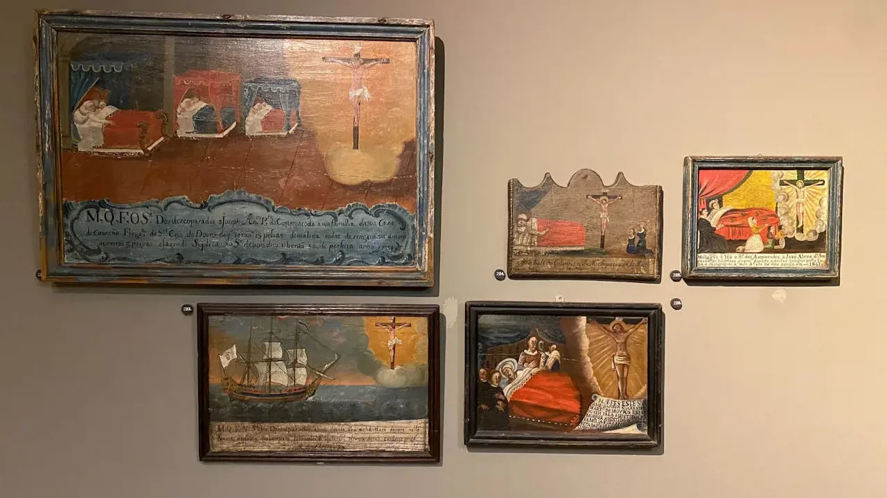 Several framed religious paintings hang on a light beige wall at Clérigos Tower & Museum Ticket.