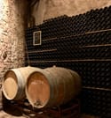 Two big wine barrels are placed in front of a shelf with hundreds of Champagne bottles 