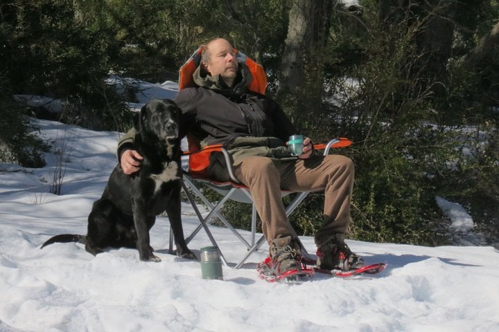 Guest resting in a camp chair in the snowy lenga forest during the San Martín de los Andes 4x4 tour, with a dog by their side