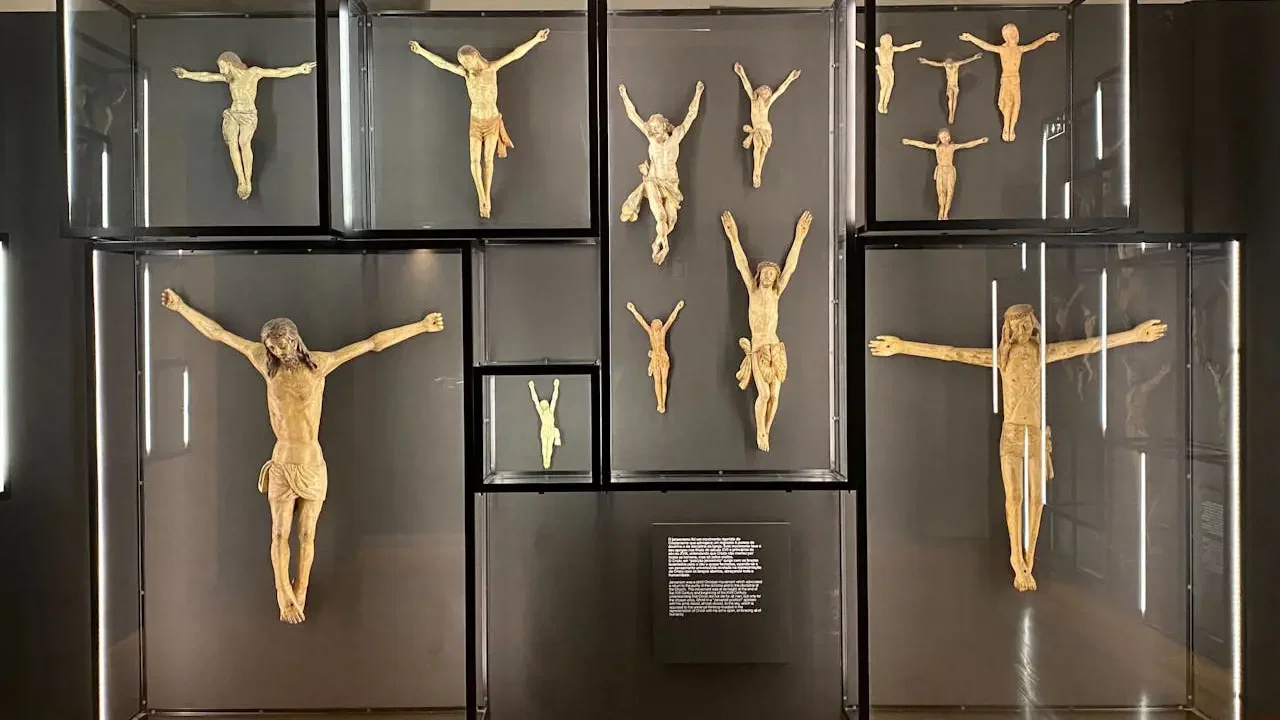 Multiple wooden crucifix sculptures are displayed inside illuminated glass wall cases at Clérigos Tower & Museum Ticket.
