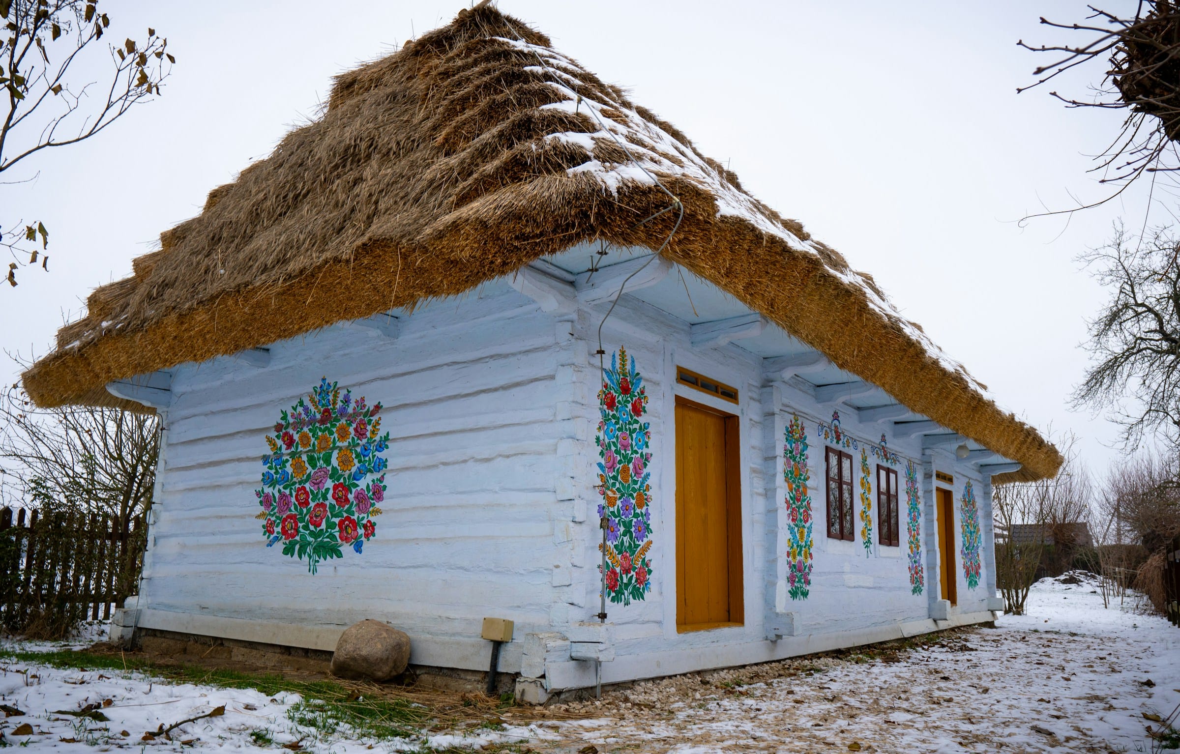 Zalipie painted cottage winter snow — white house with colourful floral folk motifs thatched roof Poland