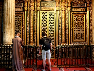 Visitors admiring the intricate golden minbar and geometric Islamic craftsmanship inside a historic Cairo mosque.