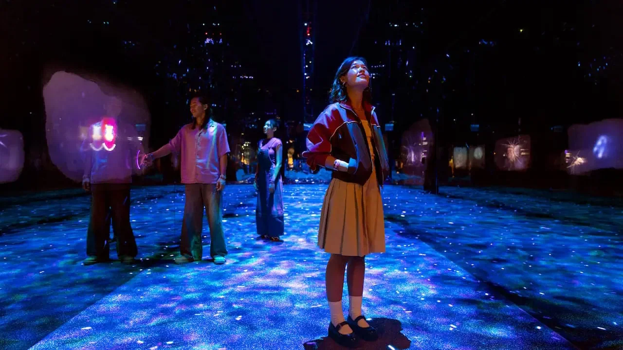 Several visitors stand in a dark room with a glowing blue projection floor and colorful displays at Exploria in Mandai Singapore Ticket.
